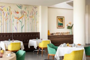 Breakfast room with set tables, colorful chairs and decorative wall, ideal to start the day in Liguria - Hotel Al Sant'Andrea, BZAR hotels in Liguria